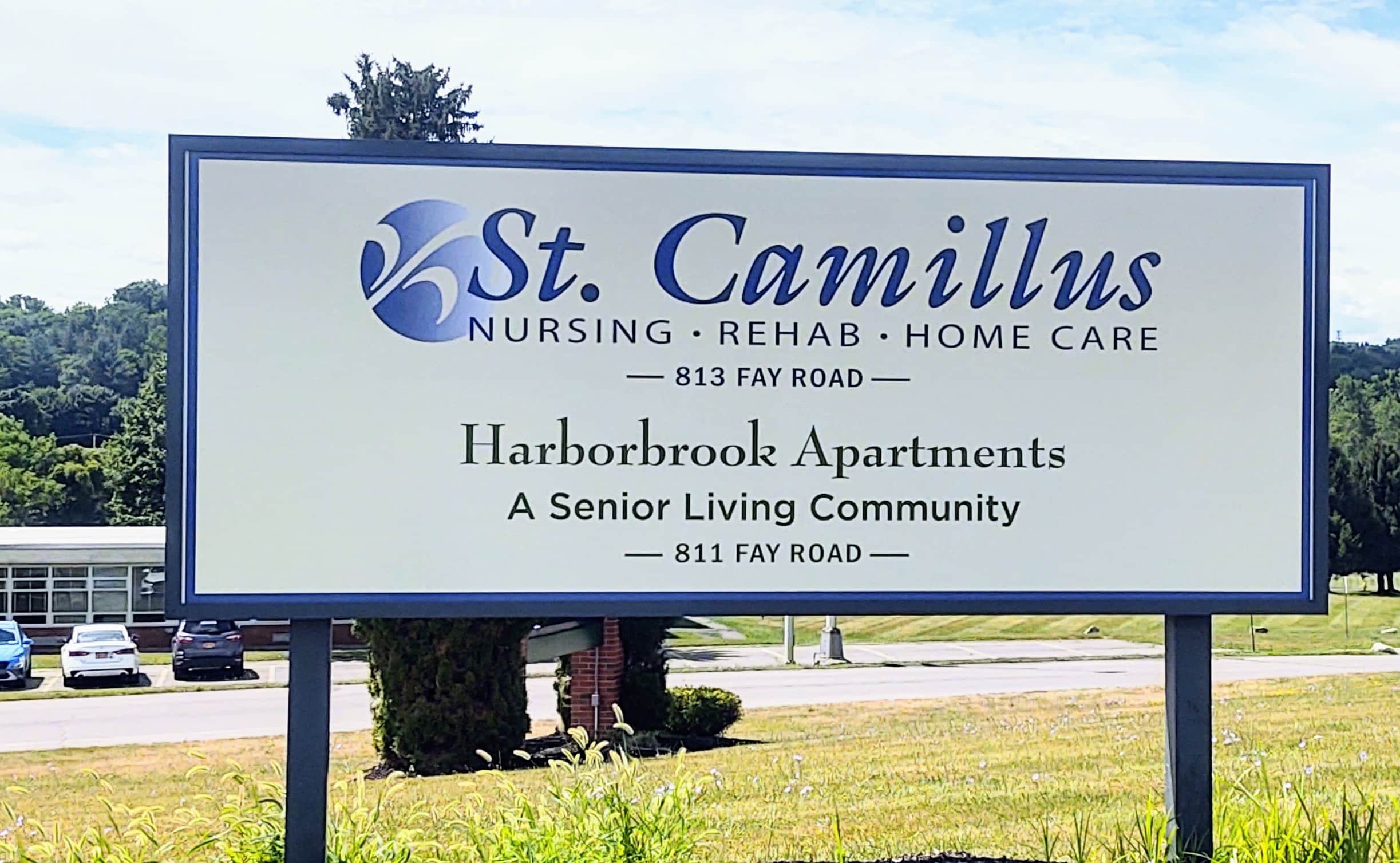 Photo with text: Sign for St. Camillus Nursing, Rehab, and Harborbrook Apartments, a senior living community, located on Fay Road.